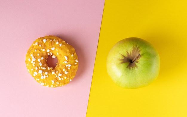 A donut and an apple on pink and yellow background diet concept