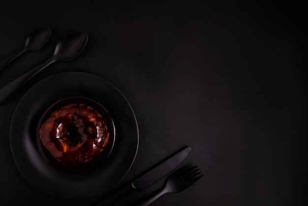 Photo donut on a black plate with black cutlery on a black background, top view