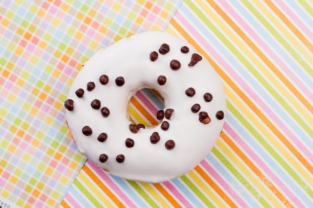 Foto ciambella su sfondo di carta colorata. ciambella glassata bianca con croccantini al cioccolato. spuntino appena sfornato.