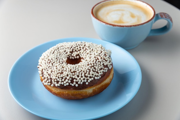 Donut covered with chocolate glaze and white sprinkles on blue plate and cup of cappuccino