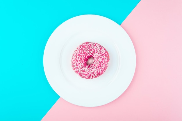 Donut covered with icing in plate top view Photo in a pink and blue color scheme
