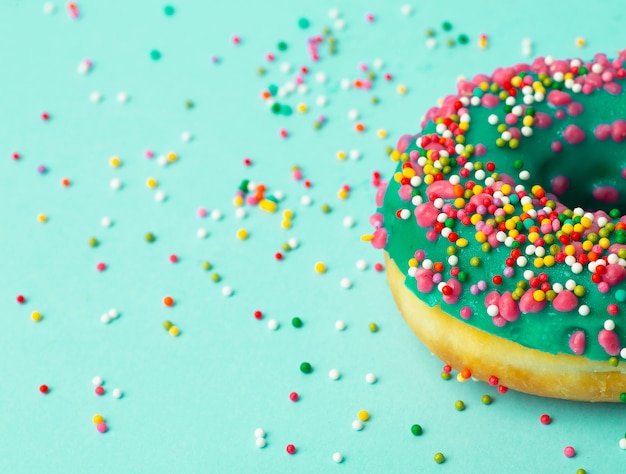 Foto ciambella (ciambella) di diversi colori su uno sfondo verde con granelli di zucchero festivo multicolore. vacanze e dolci, cottura per bambini, concetto di zucchero