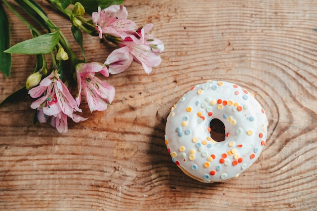 Donut en Alstroemeria bloemen op een houten achtergrond. Uitzicht van boven. donut in wit glazuur en snoep, op een houten tafel met bloemen.