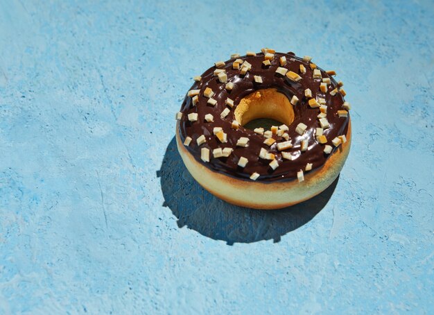Donut met chocolade glazuur en hagelslag op blauwe achtergrond.