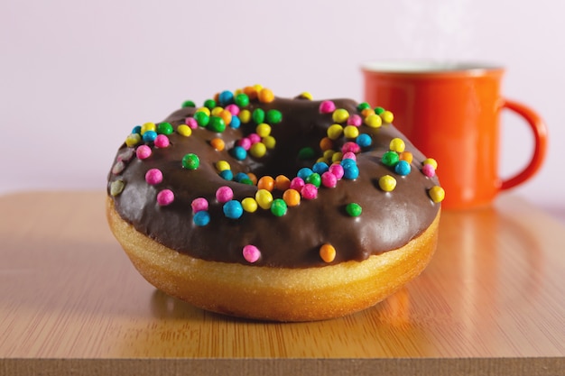 Donut met oranje koffiekopje op de achtergrond op houten voet.