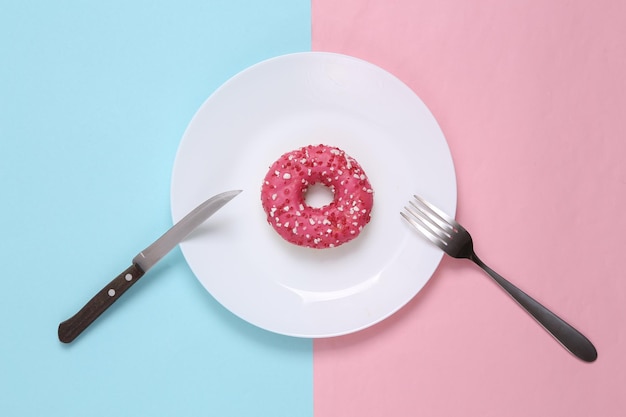 Donut op een bord met een mes en vork Blauwroze pastelachtergrond Dessert