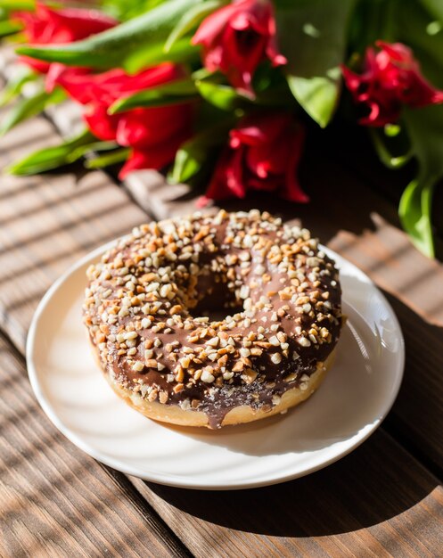 Donut op wit bord met tulpen op een bruin houten oppervlak. Ontbijt in de zomer