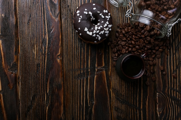 Photo donut with black icing and chocolate powder and an authentic cup of strong coffee. a can of coffee beans and poured grains.