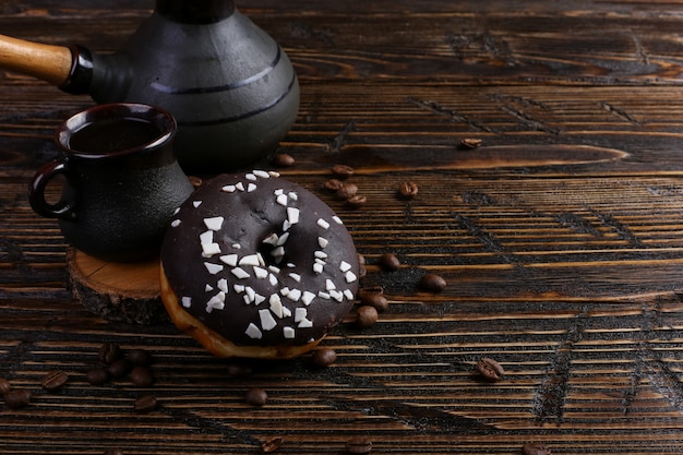 Donut with black icing and chocolate powder and an authentic cup of strong coffee. A can of coffee beans and poured grains.