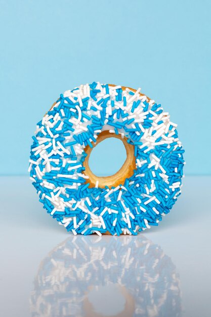 Photo donut with blue and white sprinkles on blue background with reflection and copy space for text