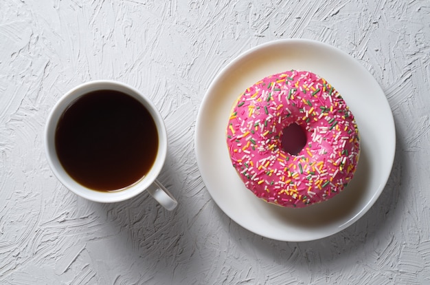 Donut with colorful icing and cup of coffee on light gray stone background