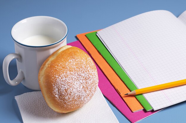 탁자 위에 우유 한 컵과 학교 공책이 있는 도넛