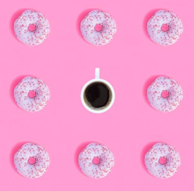 Фото Пончик с розовой глазурью и кофейной чашкой на розовом фоне плоский узор вид сверху