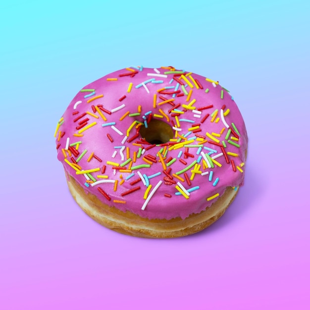 Donut with pink glaze and icing on pink and blue gradiented background. Fashion minimalism style. Flat lay view