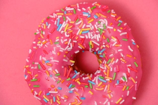 Donut with pink icing and multicolored sugar sprinklesOn pink background