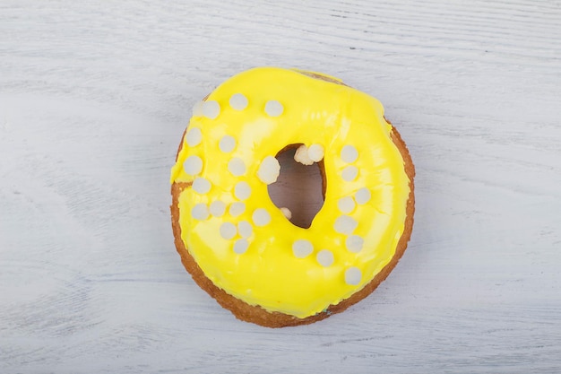 Donut with yellow glaze on white wooden background