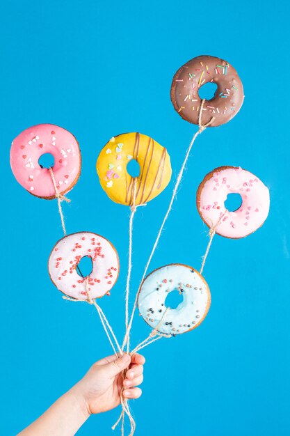 Donuts as balloons in child hand on blue background. Happy birthday party. Funny concept.