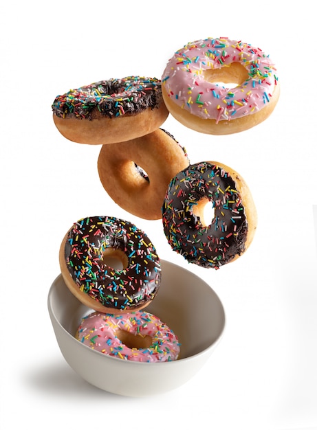 Donuts decorated with colorful sparks flying in white bowl, isolated