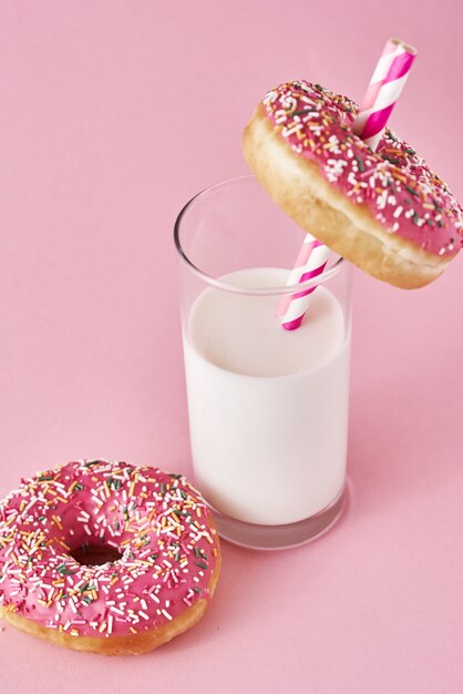 Donuts decorated with icing and sprinkle and glass of milk on pink