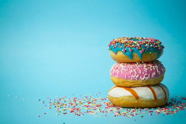 Donuts (doughnuts) of different colors on a blue background with multi-colored festive sugar sprinkles. Holiday and sweets, baking for children, sugar concept