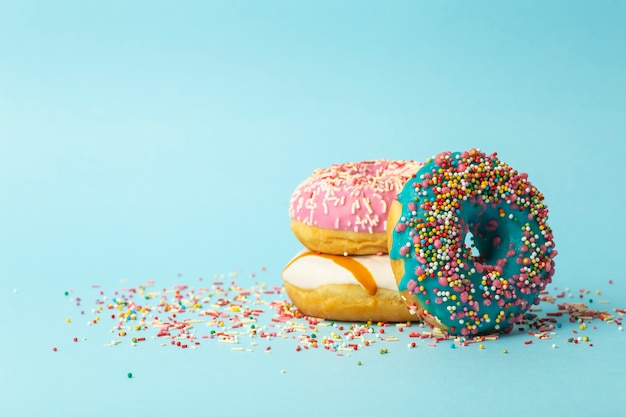 멀티 축제 설탕 뿌리와 파란색 배경에 다른 색상의 도넛 (도넛 형). 휴일과 과자, 어린이를위한 베이킹, 설탕 개념