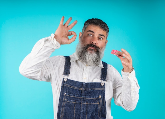 Donuts eten gebakken goederen. snoep en gebak. junk food. gebaarde hipster met blauwe borstplaat die met zijn hand gesturing terwijl zoete donuts op lichtblauw proeft.