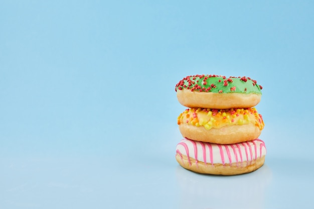 Donuts glazed with sprinkles on pastel blue background. Sweet doughnuts on blue paper. Close up.