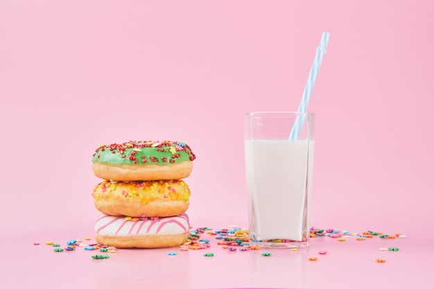 Donuts icing sprinkles with glass of milk on a pastel pink background