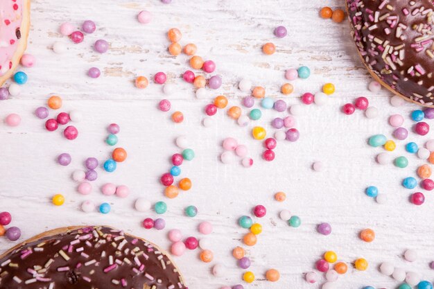 Фото Пончики в черной тарелке и сладкие конфеты на белом деревянном фоне. вкусная нездоровая еда