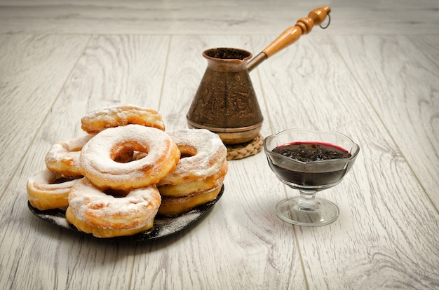 Donuts in poedersuiker, cezve koffie en bessenjam op een houten achtergrond