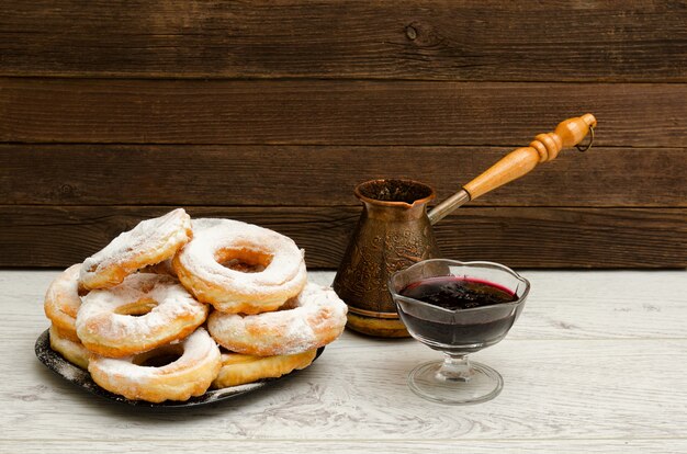 Donuts in poedersuiker, cezve koffie en bessenjam op een houten achtergrond