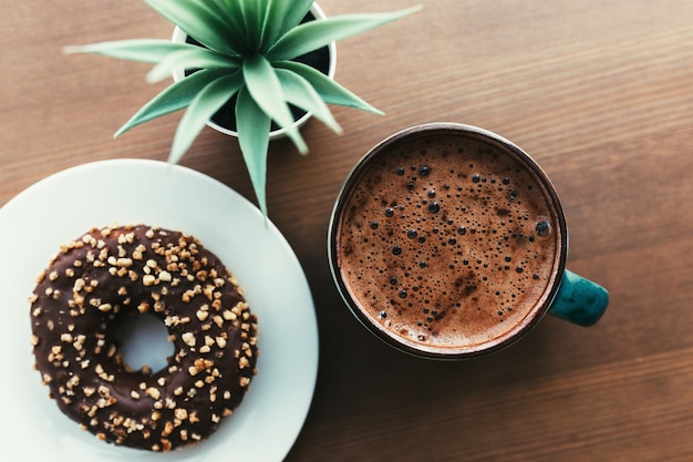 Donuts op de witte plaat, koffie en groene plant op de houten tafel