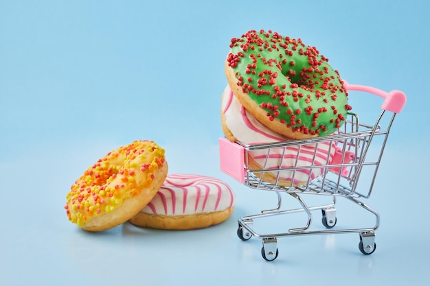 Donuts op klein winkelwagentje Winkelwagentje en geglazuurde donut op blauwe pastelachtergrond