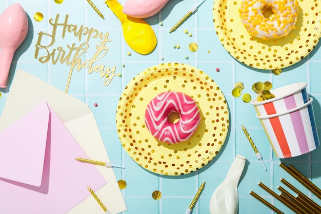 Donuts on plates and party supplies on blue background top view