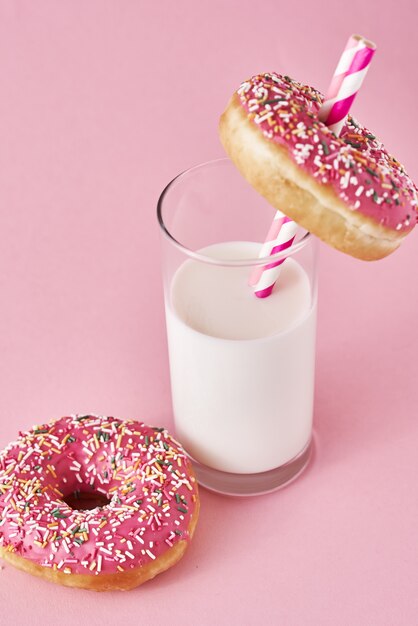 Donuts versierd met glazuur en strooi en glas melk op roze