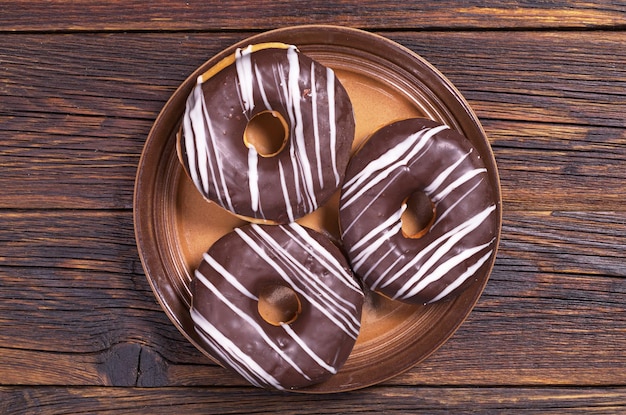 어두운 나무 배경 상단 보기에 접시에 초콜릿을 넣은 도넛
