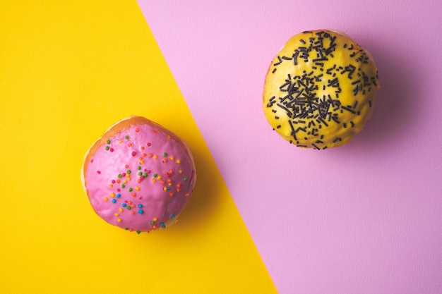 Donuts with colored icing on a yellow and pink paper background