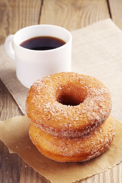 Donuts with sugar and cup of coffee on wooden table