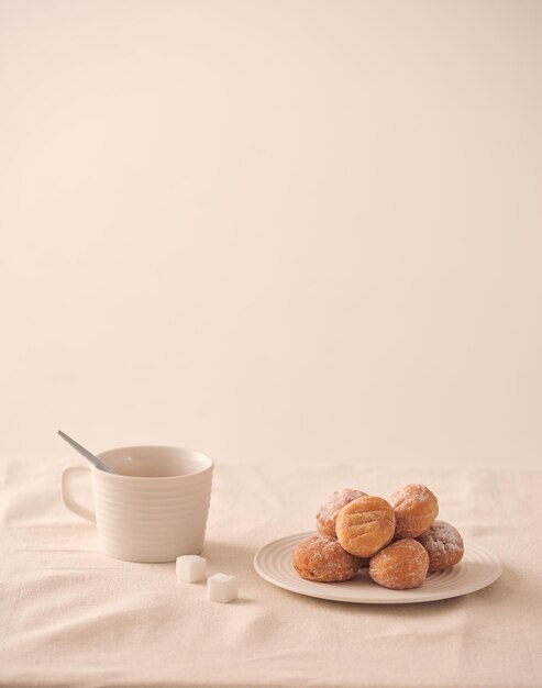 Пончики с сахаром на тарелке и чашке кофе на белом фоне