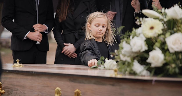 Foto dood verdriet en meisje op de begrafenis met bloem op de kist familie en verdrietig kind op de dienst op het kerkhof voor respect rozen verlies en mensen bij houten kist op de begraafplaats met kind huilen bij het graf voor begrafenisonderhouding