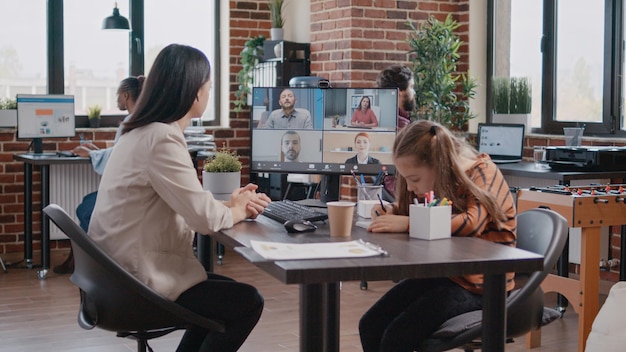 Рисует маленькую девочку на ноутбуке, пока мать-одиночка работает в офисе, разговаривает по видеосвязи с коллегами. Работающая мать посещает деловую встречу по онлайн-видеоконференции, имея ребенка в офисе