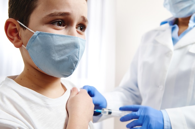 Doodsbang jongen gevaccineerd op achtergrond van wazig arts in handschoenen en witte medische jurk