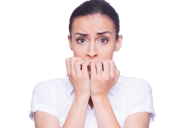 Doodsbange vrouw. Doodsbange jonge vrouw in formalwear die naar de camera kijkt en nagels bijt terwijl ze geïsoleerd op wit staat