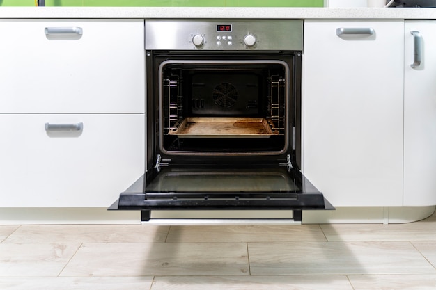 Photo the door of a dirty oven is open in a bright kitchen.