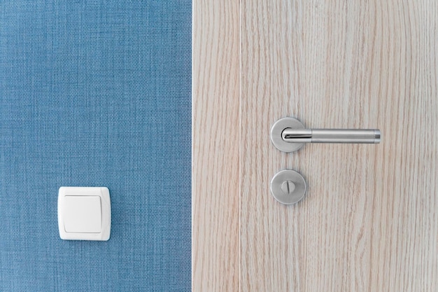 Door handle and inner lock on a wooden doors with a light switcher on a blue wall