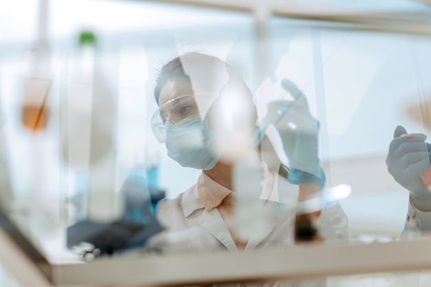 Door het glas. vrouwelijke wetenschapper zit aan een laboratoriumtafel.