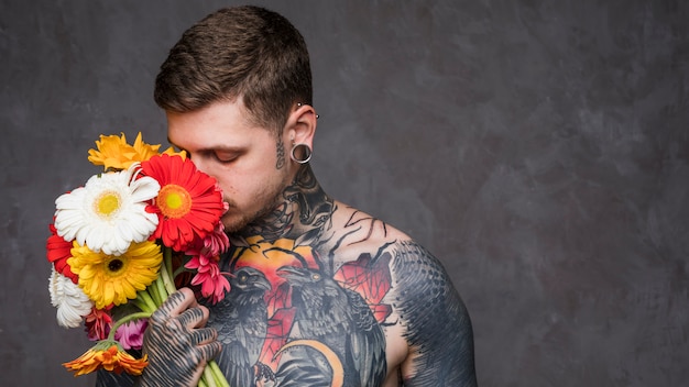Foto doorboorde jonge mens met tatoegering op zijn lichaam die de mooie gerberabloem ruiken