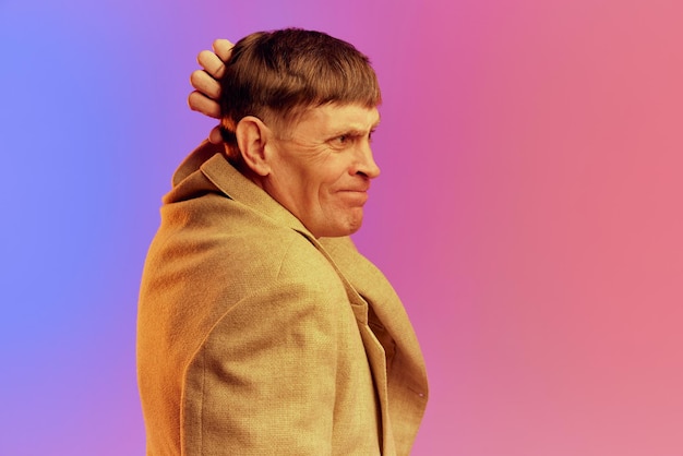 Doordachte expressie portret van volwassen man van middelbare leeftijd in jas poseren over gradiënt roze paars