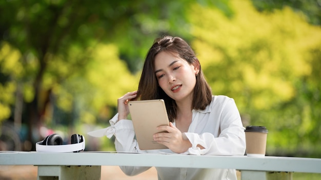 Doordachte glimlach vrouw in park met behulp van slimme digitale tablet portret van een jong charmant bedrijf