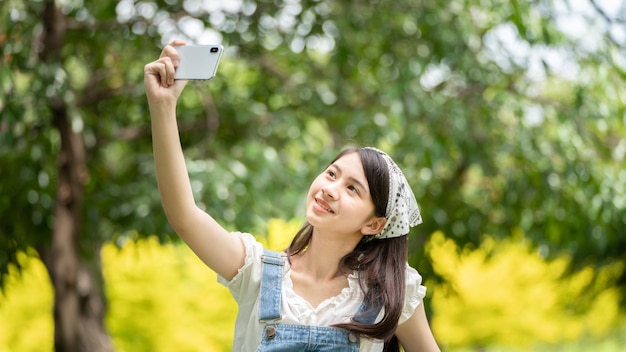 Doordachte glimlach vrouw in park met behulp van slimme telefoon voor selfie foto Portret van een jonge charmante